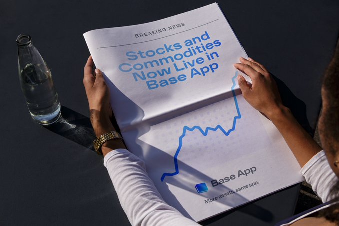 A person holds open a newspaper displaying a "BREAKING NEWS" announcement for Base App, reading "Stocks and Commodities Now Live in Base App" alongside an upward-trending stock chart and the tagline "More assets. Same app." The image illustrates the post's message by showcasing how the Base App unifies trading of diverse assets like gold, Apple stock, and Ethereum within a single platform.
