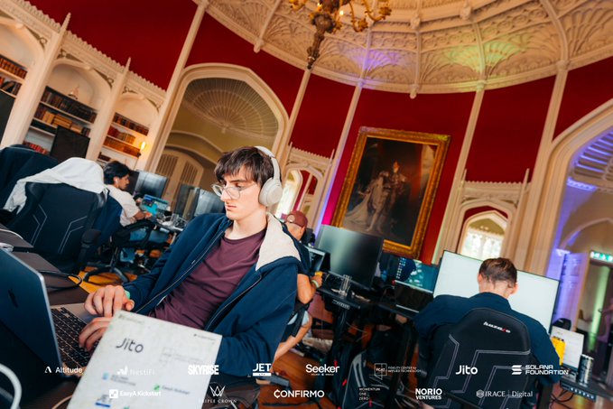 A young man with glasses and headphones sits at a laptop in an ornate room, with sponsor logos including Jito, Altitude, Solana Foundation, Skybridge, Confirme, and Nori Partners visible.