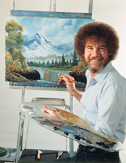 The famous painter Bob Ross smiles while holding a palette and brush in front of an easel displaying a mountain landscape painting.
