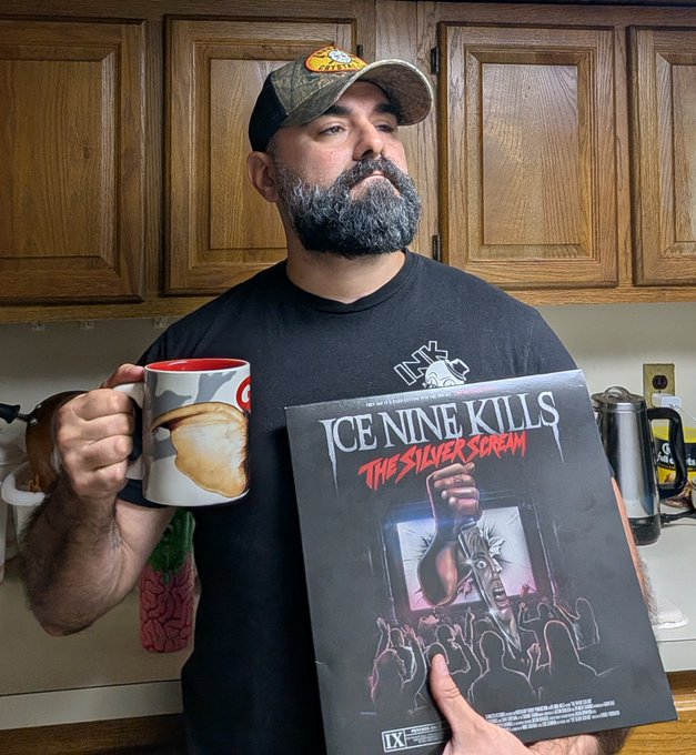 A bearded man wearing a Bass Pro Shops cap holds a mug and an 'Ice Nine Kills: The Silver Scream' horror movie-style poster.