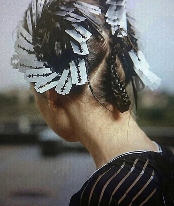 A woman from behind with her hair sectioned and held with numerous silver hair clips, wearing a striped shirt.