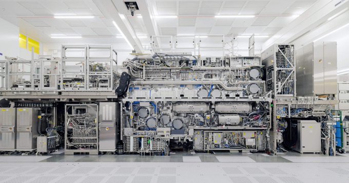 A large-scale industrial semiconductor manufacturing machine with complex piping, wiring, and processing chambers sits in a clean white facility.