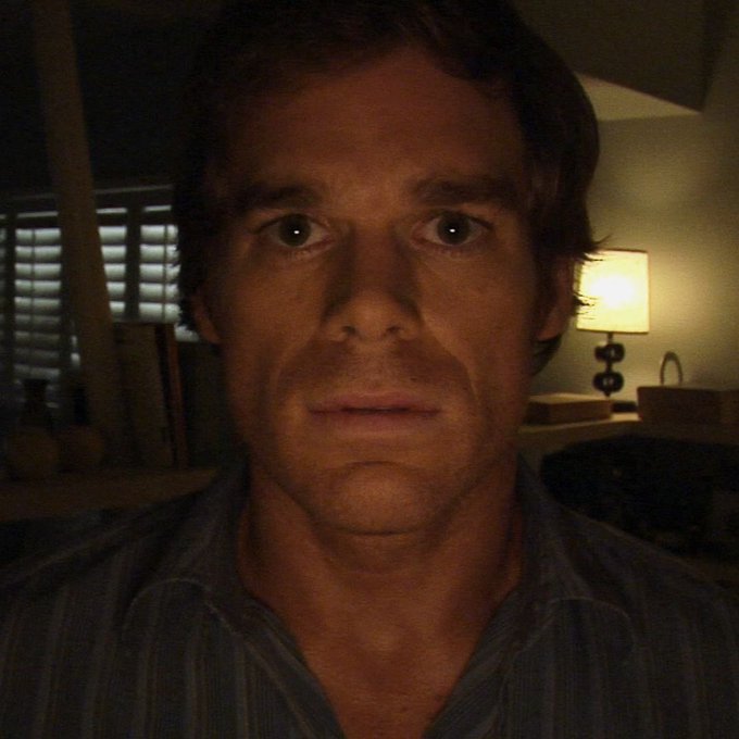 A close-up of a man's face in a dimly lit room, with a lamp visible in the background.
