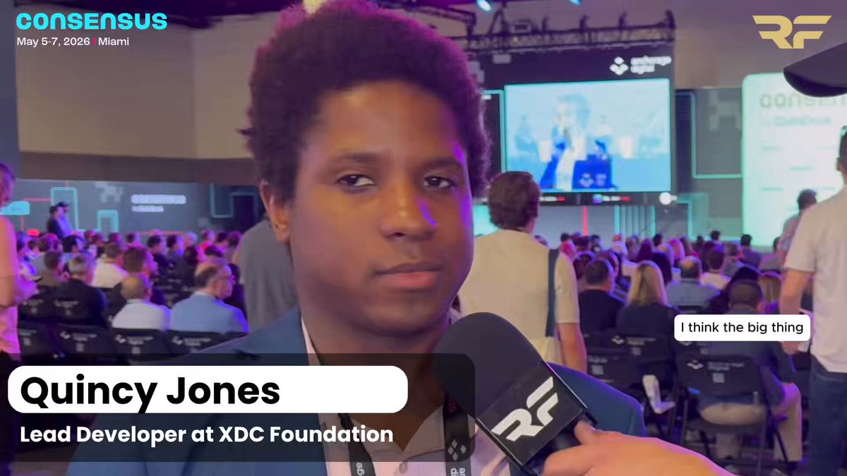The image features a young man with an afro hairstyle, wearing a suit, standing behind a microphone as he speaks into it. The background of the image shows a large crowd of people gathered for an event or conference. The caption on the image reads "Regulation, not tech, is crypto'S next frontier! @YourBroQuincy (Lead Dev at XDCFoundation) says clear rules are CRITICAL for mainstream adoption and institutional onboarding. We dive into liquidity, AI, & why the 'Wild West' is over."