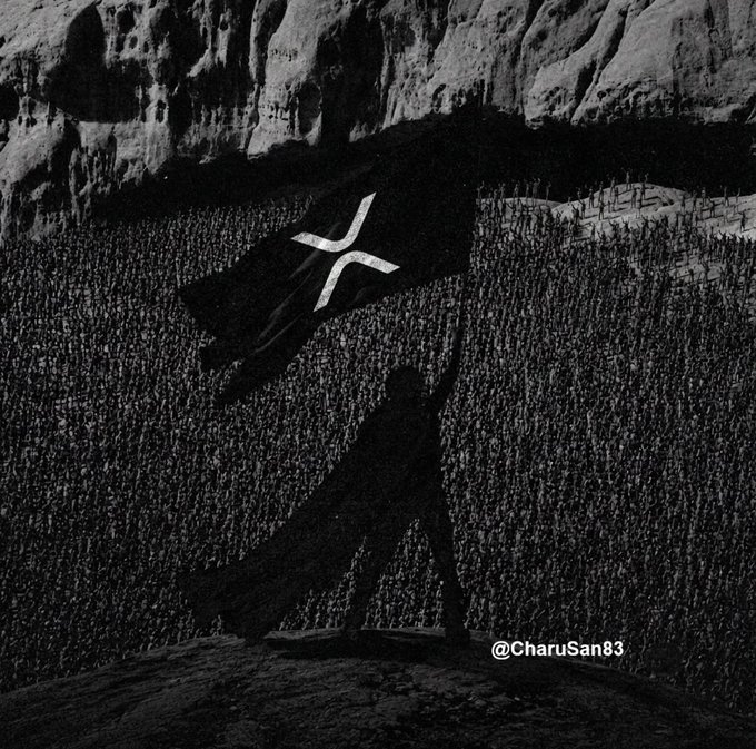 A massive crowd stretches toward towering rock formations as a giant XRP flag waves above them, casting a long shadow over the gathering. The watermark "@CharuSan83" appears in the lower right, with the scene evoking the dramatic scale of the XRP community rallying behind the cryptocurrency.
