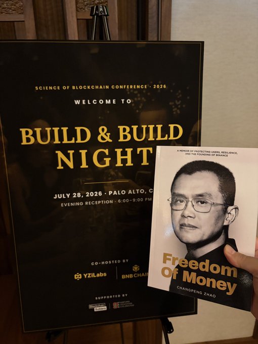 A welcome sign for the 'Science of Blockchain Conference 2026 Build & Build Night' on July 28, 2026 in Palo Alto, co-hosted by YZiLabs and BNB Chain, with a hand holding Changpeng Zhao's memoir 'Freedom of Money' in the foreground.