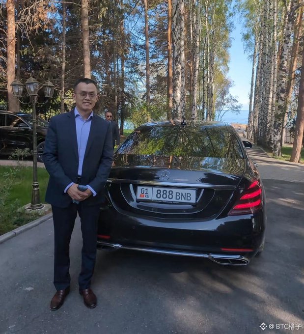 A man in a blue suit standing next to a black Mercedes-Benz with the license plate '888 BNB', with the watermark 'BTC格子' visible.
