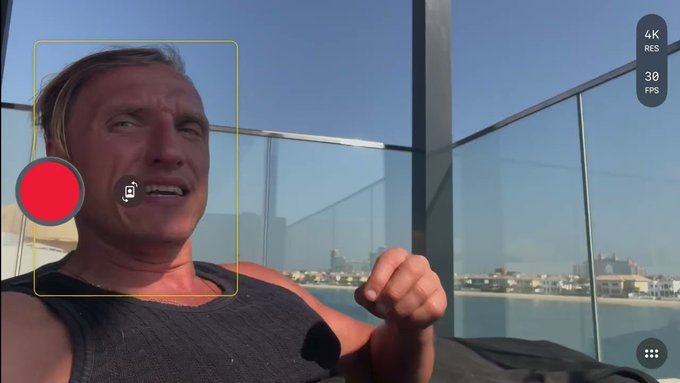 A close-up of a man on a sunny balcony is framed by a yellow face-detection box, with a large red record button and a small camera icon over his cheek. A smartphone camera UI shows “4K,” “RES,” and “30 FPS,” while the post text reads, “Bitcoin is about to MELT Faces………. youtu.be/UBMPJYiDIr0,” framing his strained expression as part of a bullish Bitcoin reaction.