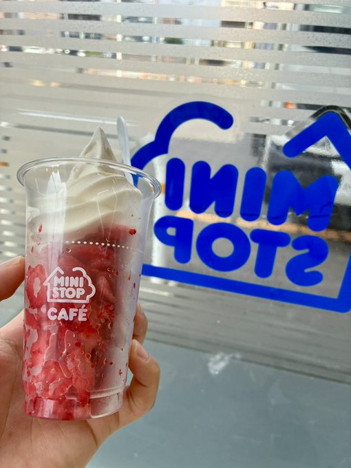 A hand holds a Ministop Café cup filled with a strawberry dessert and soft-serve ice cream, photographed in front of a Ministop storefront with the blue "MINI STOP" logo visible on the window.

The image perfectly matches the post—it's the exact "Ministop" the author happily stumbled upon while walking near their home, with the café cup showcasing the sweet treat they picked up during their stroll.