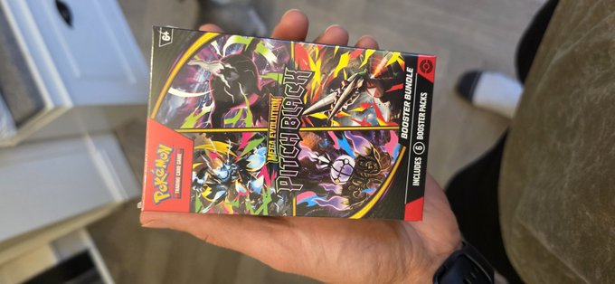A hand holds a sealed Pokémon Trading Card Game booster bundle, specifically the Surging Sparks set containing 6 booster packs.