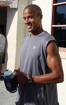 A smiling, muscular man in a sleeveless gray shirt holds a water bottle while standing outside a building. The post references $NBIS, suggesting the image relates to the stock ticker symbol or company associated with this individual.