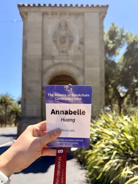 A hand holds up an "SBC '26" (Stanford Blockchain Conference) name badge for "Annabelle Huang" (Hivemind Labs) in front of a stone archway at Stanford, visually marking the author's attendance at their 4th conference despite the notably smaller turnout.