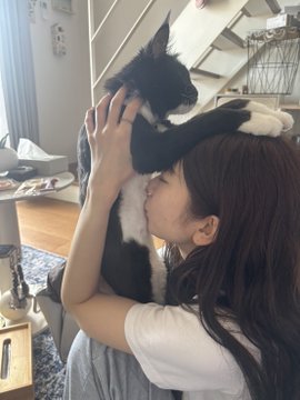 A young woman affectionately hugs a black and white border collie-type dog, resting her cheek against the dog's fur in a cozy indoor setting.