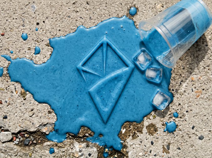 A close-up image of spilled blue liquid forming the Ethereum logo on concrete next to a tipped plastic cup with ice.