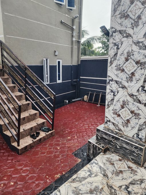 A photo of a building exterior with a red tiled floor, a staircase with metal railings, and marble-patterned columns and steps.