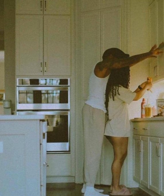 A couple shares a tender embrace in a sunlit kitchen, embodying the warmth and gratitude expressed in the post about a blessed Sunday and progress within their community.