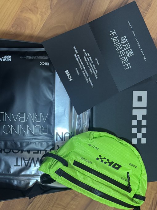 An unboxing shows OKX merchandise including a silver 'Running Armband' package, a black instruction booklet titled 'ARMBAND FITTED GUIDE,' and a bright neon green running belt laid out on a wooden surface.
