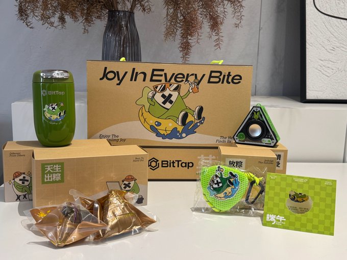 The image features a collection of items, including boxes containing various products such as a green cup with a cartoon character design, a box of cookies, and a small gift bag. The objects are arranged on a table or countertop, creating an appealing display for potential buyers. The post encourages people to unwrap the zongzi (Chinese fortune teller) and enjoy it for good luck and fortune. The image also includes a social media code "@grok" that could be used by fans to enter a contest or giveaway related to the products featured in the image, such as winning a gift bag from BitTap.