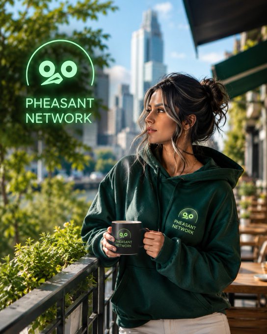 A woman in a green 'Pheasant Network' hoodie holds a matching branded coffee mug on a balcony with a city skyline in the background.