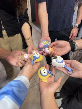 Five people hold up various small collectible figurines in the center, bringing them together in a circle.