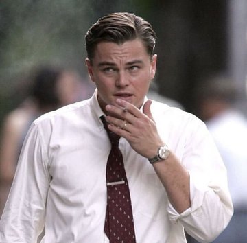 A photograph of actor Leonardo DiCaprio wearing a white shirt and dark tie, with his hand near his mouth in a thoughtful expression.