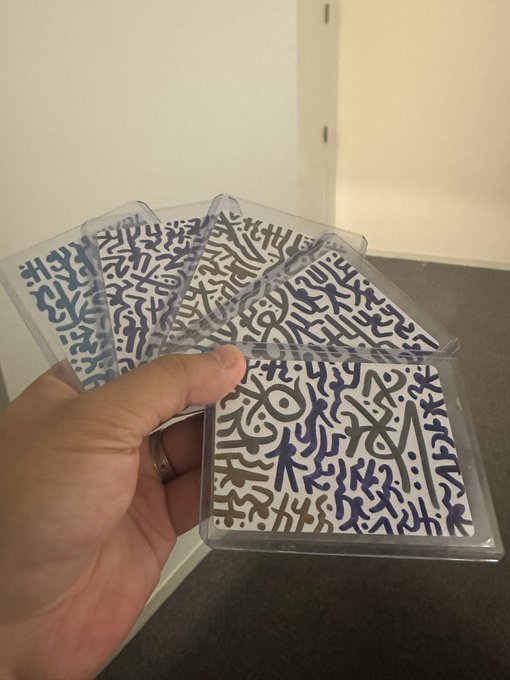 A hand holding a fan of trading cards in plastic sleeves featuring an abstract squiggly black-and-white pattern design.