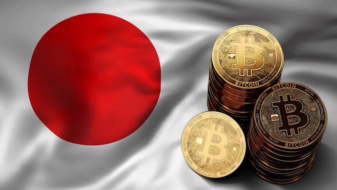 The flag of Japan is displayed alongside several stacks of gold Bitcoin coins.