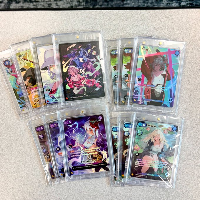 A collection of trading cards featuring anime characters (including 'Mobby', 'Shao', 'Thunderclap', and 'Mizuki') displayed in protective sleeves on a surface.