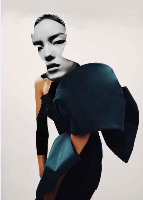 Editorial fashion photo featuring a model wearing an avant-garde dark teal sculptural garment paired with a smooth white mask covering the upper half of her face.