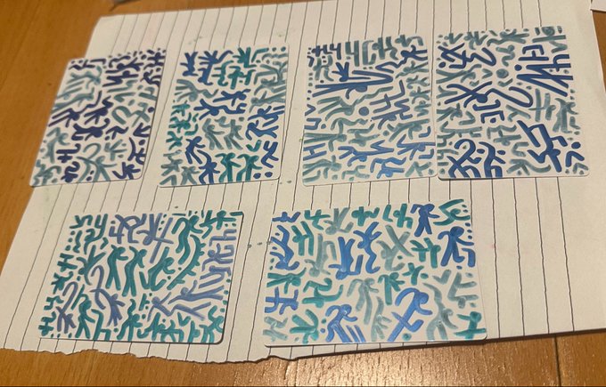 Five rectangular cards with abstract scribble patterns in blue and green tones laid out on a wooden table.