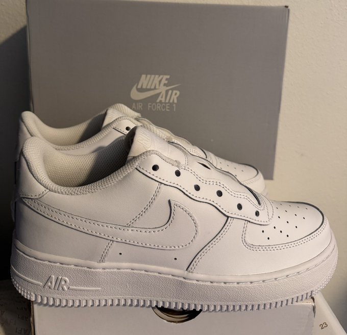 A pair of white Nike Air Force 1 sneakers sits in front of a grey Nike Air Force 1 shoebox.