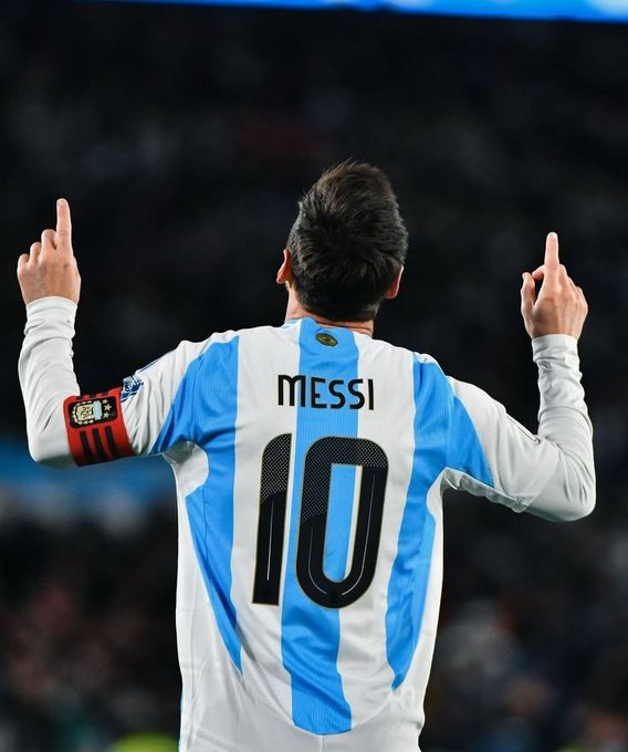 Lionel Messi wearing the Argentina #10 jersey from behind, pointing both index fingers upward toward the sky during a match.