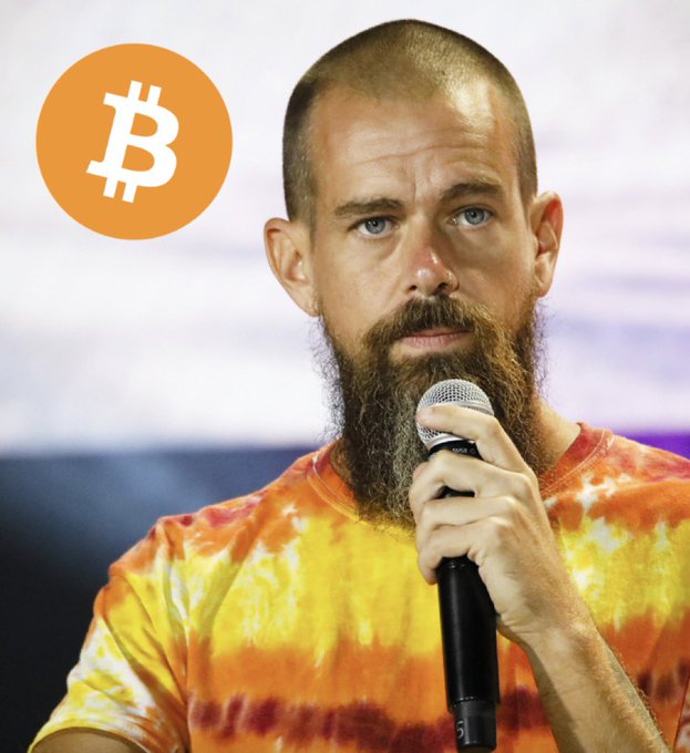 A bearded man in a tie-dye shirt speaks into a microphone, with a Bitcoin logo displayed in the upper left corner, illustrating Jack Dorsey's announcement that Block's Square Credit Card holders will soon earn 3% back in Bitcoin.
