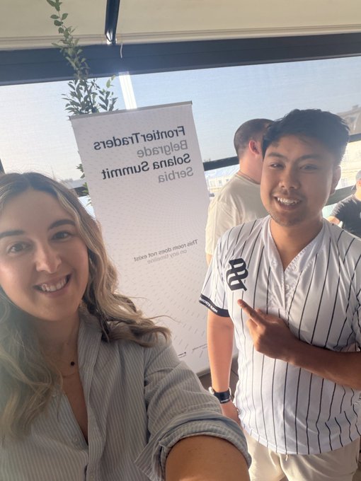 A selfie of two smiling people posing in front of a whiteboard that reads 'Frontier Traders Beliefs Summit Solids Summit' in mirrored text.