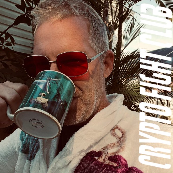 The image features a man wearing sunglasses, a robe or bathrobe, and holding a mug with a picture of an alien on it. The background includes palm trees and a house, suggesting a tropical location. The caption reads "Gm. Yup just waking up. Spaces until 3am will do that." This implies the man is in bed and has not yet started his day or engaged in any activities.