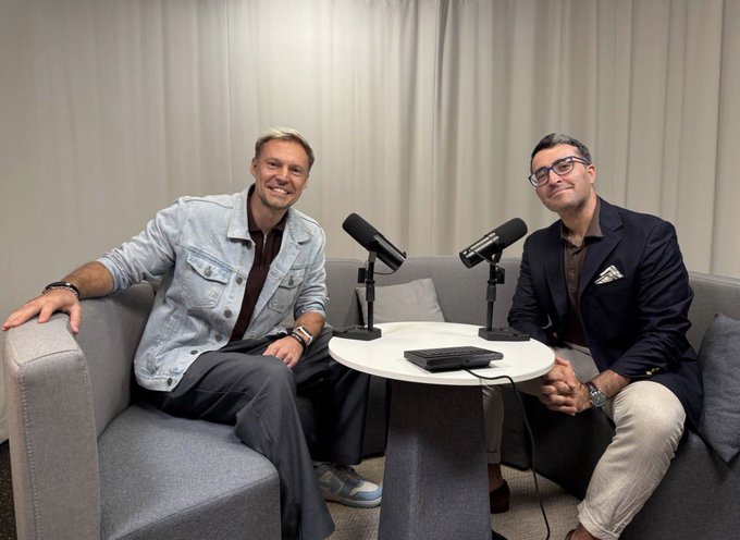 Two well-dressed men sit smiling on a gray couch during a podcast recording, with professional microphones and a small round table between them. The caption reflects a relaxed interview setting in Singapore, likely featuring a guest discussing crypto market structure trends with the Finery Markets podcast.