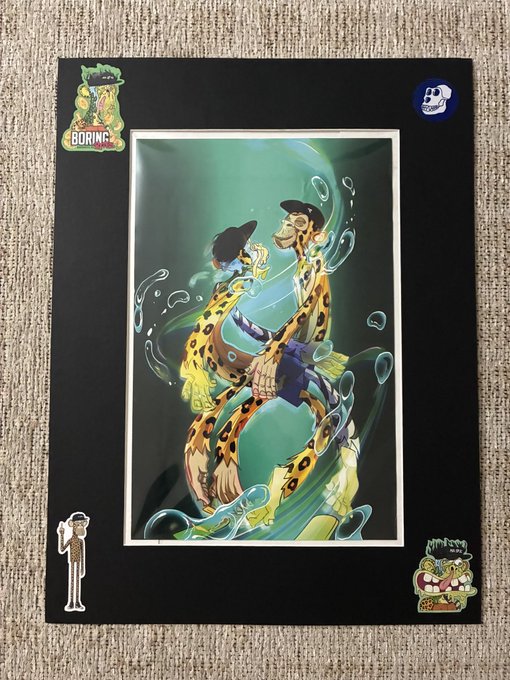 A framed anime-style art print of two leopard-print humanoid characters underwater, displayed against a black mat with decorative stickers, resting on a carpet.
