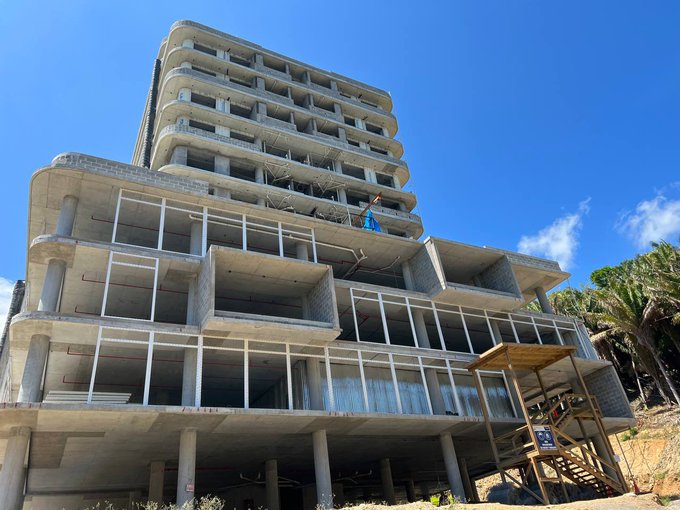 The image shows an unfinished building under construction, with a person standing on top of the structure. The building appears to be made of concrete or cement blocks, giving it a modern and industrial look. In the background, there are palm trees visible, adding a tropical feel to the scene. The post about the economic zone in Honduras is related to this image because the construction site could potentially be part of an early bitcoin-inspired economic zone that was established in 2013. This area aimed to provide financial services and support for Bitcoin transactions using blockchain technology.