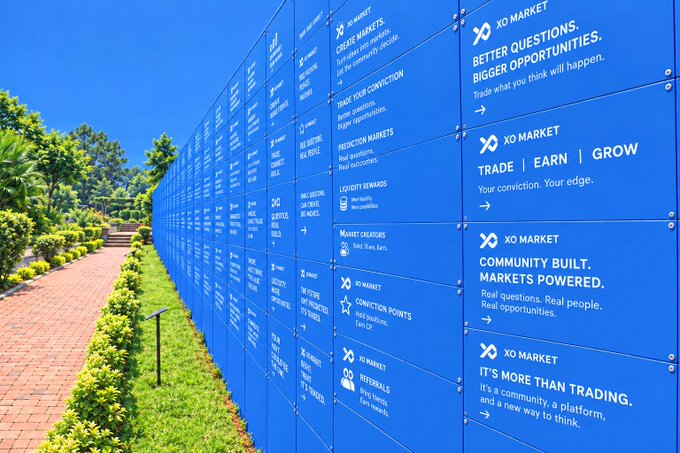 A long outdoor display of blue signs for 'XO Market' lists various features including 'Create Markets', 'Trade Your Conviction', 'Prediction Markets', 'Loyalty Rewards', 'Market Creators', 'Conviction Points', 'Referrals', 'Trade | Earn | Grow', and 'Community Built, Markets Powered.'
