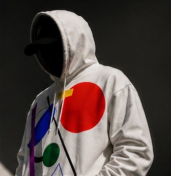 A person wearing a white hoodie with a colorful geometric logo of overlapping circles, their face obscured by the hood and a dark cap.