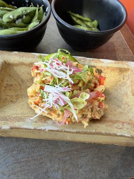 A plated dish of what appears to be tuna tartare or ceviche topped with microgreens, served on a rectangular stone plate with edamame on the side.
