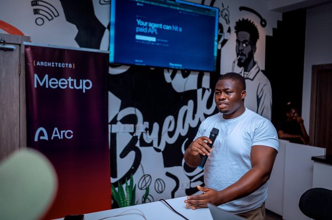 A man speaking into a microphone at an '[ARCHITECTG] Meetup' event by Arc, with a presentation screen displaying 'Your agent can hit a paid API.'