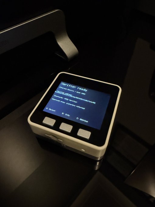 A small white hardware device with a screen displaying 'Upliftor ready' and other system text, featuring three physical buttons labeled 'A: Select', 'B: Info', and 'C: Service'.