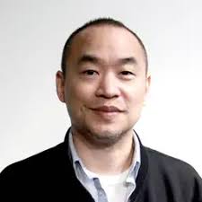 A professional headshot shows an Asian man with short dark hair wearing a black blazer over a light blue collared shirt, smiling slightly against a neutral gray background. The image appears to be a portrait of Machi Big Brother, the prominent crypto/NFT trader referenced in the post who reportedly sold a Bored Ape NFT at a substantial loss.