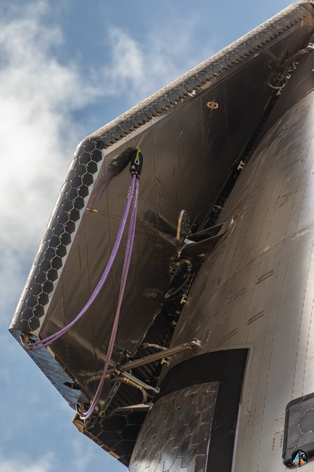The image shows the underside of SpaceX's Starship SN42 rocket, featuring its distinctive black hexagonal heat shield tiles and deployed landing legs, with purple lifting straps still attached. The post's reference to "SN42" matches the Starship prototype shown, captured during ground operations.