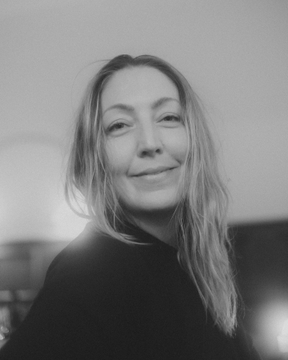 A black-and-white portrait of a smiling blonde woman against a softly lit background.