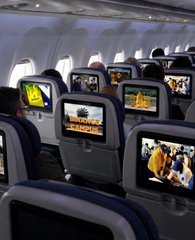 The interior of an airplane cabin with rows of seatback screens displaying various images and entertainment content.