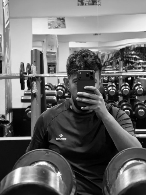 The image features a man taking a photo of himself with his cell phone while sitting at a weight bench inside a gym, surrounded by various exercise equipment such as dumbbells and barbells. The caption "My gym companion" suggests that this person is documenting their workout experience or sharing it on social media platforms.