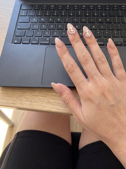 A hand with long, decorated nails rests on a laptop trackpad, showing off two fingernails with small smiley face designs in white.
