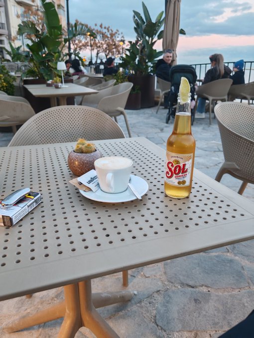 A morning coffee and a Sol beer sit on an outdoor terrace table at sunset, fitting the relaxed "good morning" vibe of the post. The Sol bottle is the only visible branding, with its label clearly readable.
